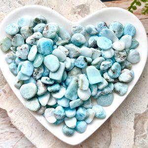 May include: A heart-shaped dish filled with a variety of light blue and white tumbled stones. The stones are smooth and have a natural, organic look.