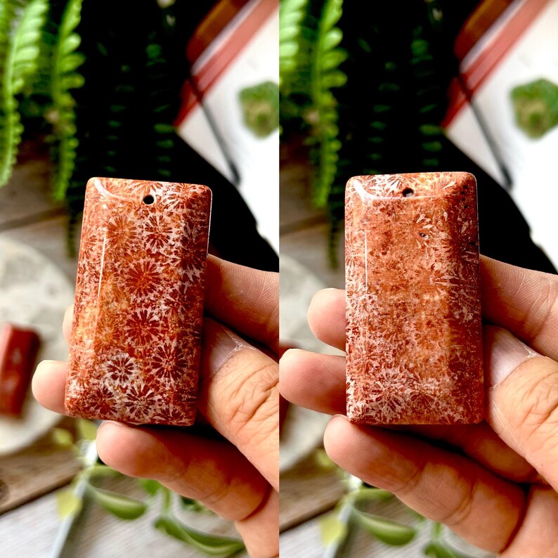 May include: Two rectangular coral pendants with a floral pattern. The pendants are a reddish-orange colour with white accents. Each pendant has a small hole at the top for stringing. The pendants are held in a person's hand.
