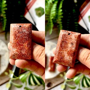 May include: Two rectangular coral pendants with a hole drilled at the top. The pendants have a reddish-brown colour with a detailed, natural pattern. The pendants are held in a person's hand.