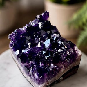 May include: A deep purple amethyst crystal cluster featuring numerous sharp, multifaceted points. The mineral specimen displays a rich violet hue with translucent edges and a solid, dark base, showcasing a natural, jagged formation of crystalline structures.