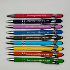 May include: A collection of nine colorful pens with silver accents and black stylus tips. Each pen has a different color barrel, including red, navy, pink, blue, brown, teal, yellow, orange, and green. The text "jensenengravables.etsy.com" is printed on each pen.
