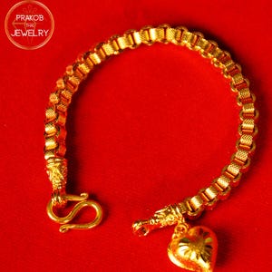 May include: A gold bracelet with a heart charm and a clasp in the shape of a hook. The bracelet is on a red background.