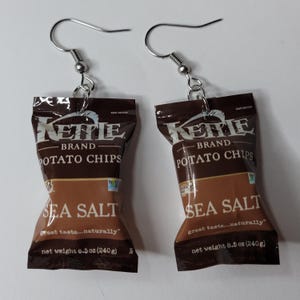 May include: A pair of earrings made from miniature bags of Kettle Brand Sea Salt potato chips. The bags are brown with white text and the earrings are silver.
