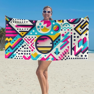 May include: A beach towel with a geometric pattern in shades of pink, blue, yellow, and white. The pattern includes circles, squares, and triangles.