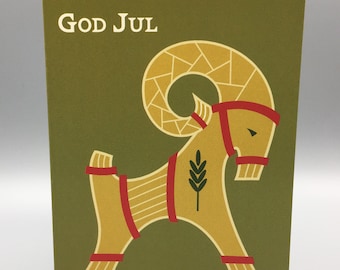 May include: A green card with the text "God Jul" in white lettering. A stylised yellow goat with red accents is depicted on the card.