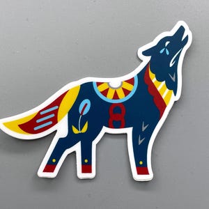 May include: A sticker featuring a stylized howling wolf. The wolf is primarily navy blue with decorative elements in yellow, red, and blue. The design includes a floral motif and the number eight.