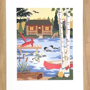 May include: A colorful print depicting a lakeside cabin scene. A red Adirondack chair sits on a wooden dock. The lake features a canoe, loons, and a turtle. Birch trees and a woodpecker are visible. The artwork evokes a sense of nature and tranquility.