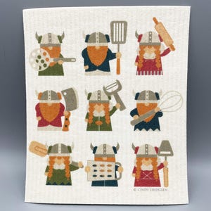 May include: A set of nine illustrated kitchen dishcloths featuring a Viking theme. Each dishcloth has a different Viking character holding a different kitchen utensil, such as a rolling pin, spatula, whisk, and more. The dishcloths are beige with a white background and have a copyright notice at the bottom.
