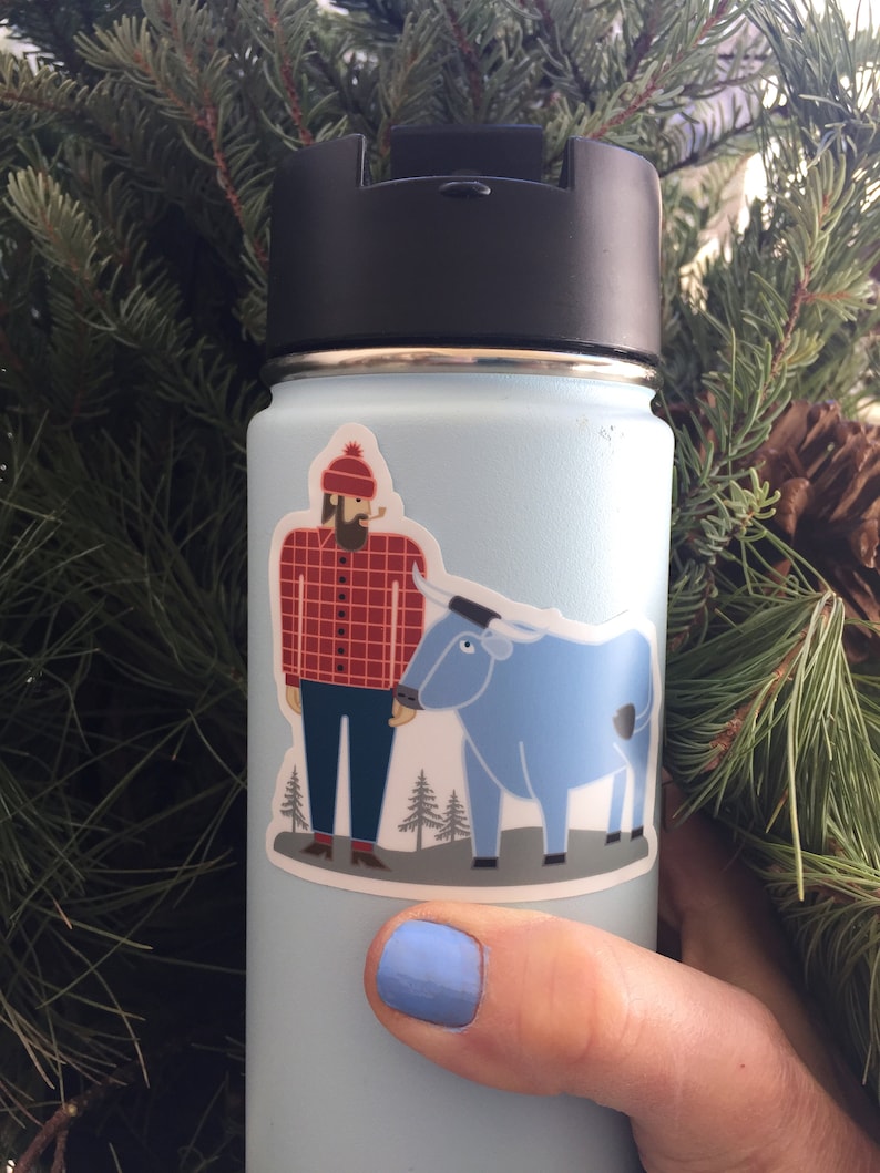 May include: A blue reusable water bottle with a sticker of a man with a beard and a red and black checked shirt standing next to a blue ox. The sticker is on the front of the bottle.
