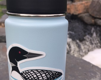 May include: A light blue reusable water bottle with a black lid and a sticker of a black and white loon with red eyes on the side.