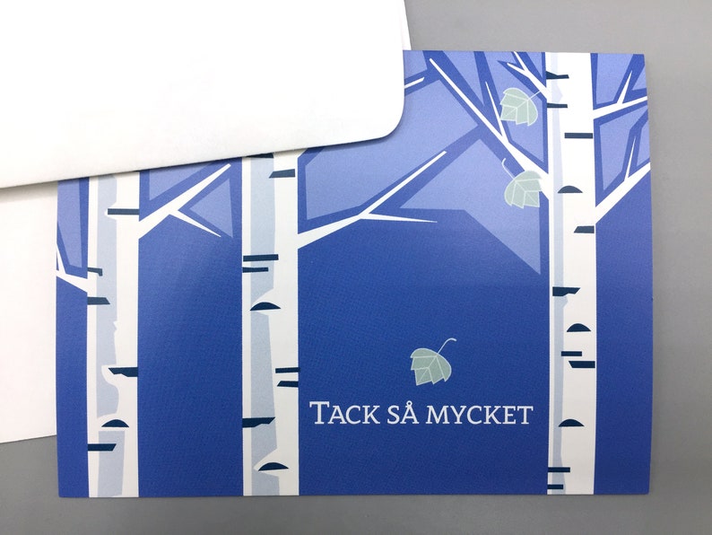 Pu&ograve; includere: Un biglietto blu con un disegno di betulla bianca e il testo "TACK S&Aring; MYCKET" in bianco.