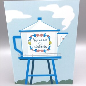 May include: A blue and white water tower with a floral wreath and the text "Välkommen till Lindström" on the side. The tower is set against a light blue sky with white clouds.