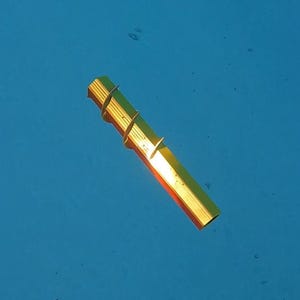 Könnte beinhalten: Ein goldfarbenes, rechteckiges Objekt mit einem Spiraldesign und Flossen, das in blauem Wasser schwimmt. Das Objekt hat einen metallischen Glanz und scheint ein dekoratives oder funktionales Element zu sein.