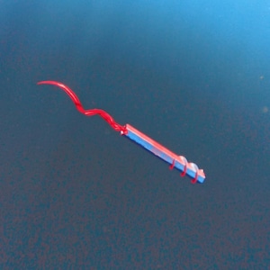 May include: A small, colorful tool with a red, wavy wire extending from a blue and red rectangular body. The tool has a spiral design wrapped around the body, and is set against a blue background.
