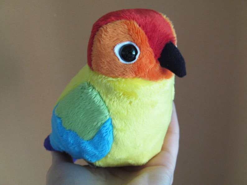 K&ouml;nnte beinhalten: Ein Pl&uuml;schtier in Form eines Vogels mit gelbem K&ouml;rper, rotem und orangefarbenem Kopf und blauen und gr&uuml;nen Fl&uuml;geln.