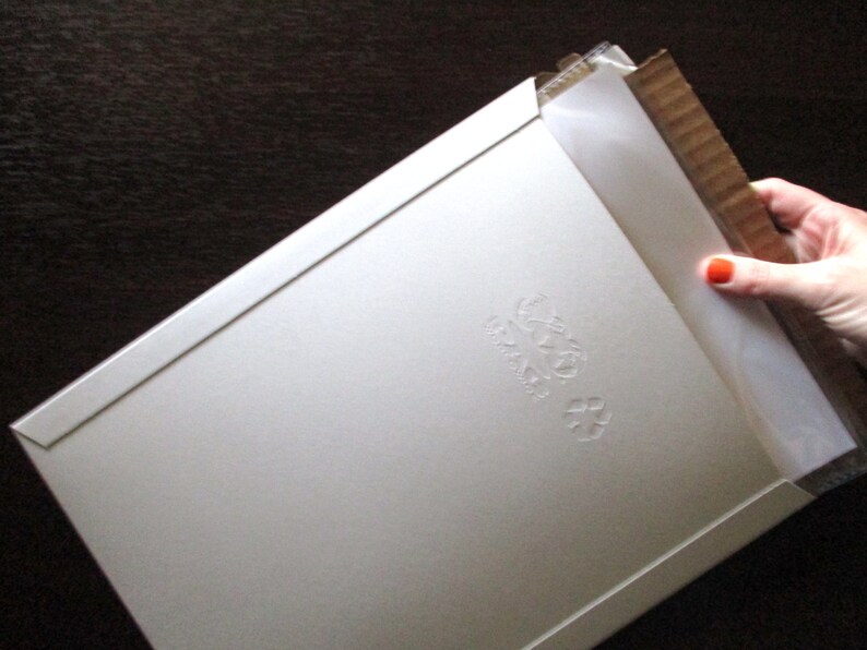Op de afbeelding: Een witte kartonnen envelop met een reli&euml;fdesign van een gestileerde bloem. De envelop is gevouwen en heeft een flap aan de bovenkant.