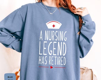 Puede incluir: Una sudadera azul con el texto "A Nursing Legend Has Retired" en blanco con un corazón rojo y una cruz roja en un gorro de enfermera blanco.