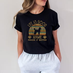 May include: Black t-shirt with a vintage sunset graphic and a silhouette of a poodle. The text "Life is good NAME makes it better" is printed on the shirt.