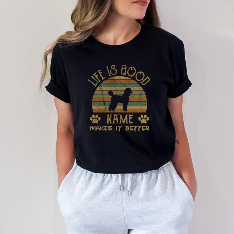 May include: Black t-shirt with a vintage sunset graphic and a silhouette of a poodle. The text "Life is good NAME makes it better" is printed on the shirt.