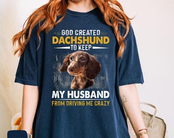 Puede incluir: Una camiseta azul marino con un gráfico de perro dachshund y el texto "Dios creó al dachshund para evitar que mi marido me vuelva loca".