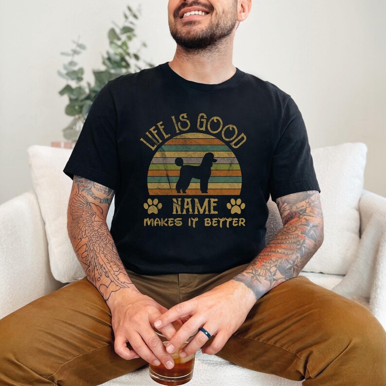 May include: A black t-shirt with a vintage-style sunset graphic and the text "Life is good [Name] makes it better". A silhouette of a poodle is in front of the sunset.