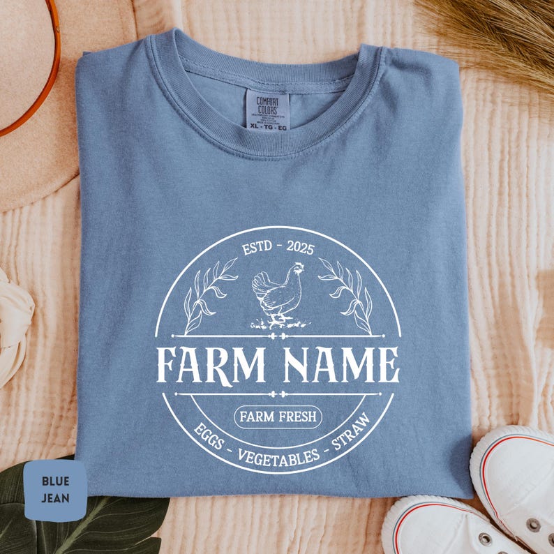 May include: A blue jean t-shirt with a white graphic of a farm logo. The logo features a chicken, the text "FARM NAME", "ESTD - 2025", "FARM FRESH", and "EGGS - VEGETABLES - STRAW".