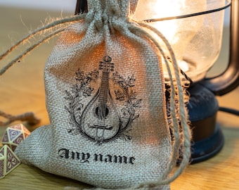 May include: A tan burlap drawstring pouch featuring a black ink illustration of a mandolin surrounded by a leafy vine wreath. The text "Any name" is printed in a gothic-style font below the instrument. The bag is made of woven fabric.