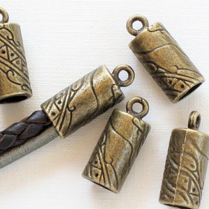 May include: Five antique gold-toned metal cord end caps with an intricate design. The caps have a loop at the top for attaching to a cord.