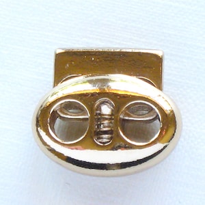 May include: Gold-toned metal toggle clasp with two oval-shaped holes. The clasp is designed for securing cords or straps.