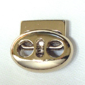 May include: Gold-toned metal toggle clasp with two holes. The clasp has a spring mechanism.