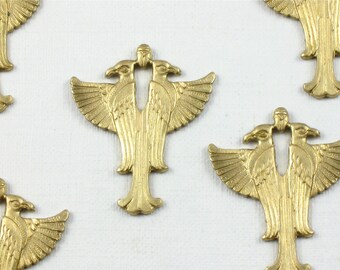 May include: Several gold-colored metal eagle charms with two heads and outstretched wings are arranged on a white surface. The charms have a detailed, embossed design and a decorative base. The overall theme is vintage or antique jewelry components.
