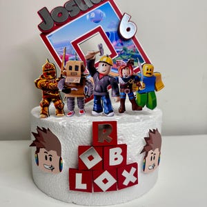Puede incluir: Un adorno para pastel con tem&aacute;tica de Roblox con el nombre "Josua" y el n&uacute;mero "6". El pastel est&aacute; decorado con figuras de personajes de Roblox y el logotipo de Roblox. El pastel es blanco con detalles en rojo y plata.
