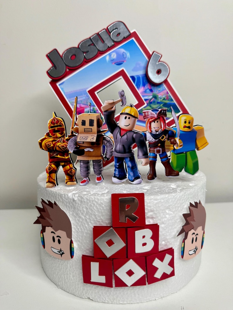 Puede incluir: Adorno para tarta con personajes de Roblox y el nombre "Josua" y el n&uacute;mero "6". La tarta est&aacute; decorada con bloques rojos que deletrean "ROBLOX" y recortes de personajes. Los personajes incluyen un caballero, un robot y otros avatares de Roblox.