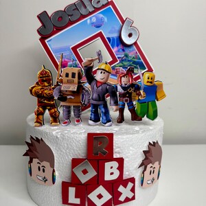 Puede incluir: Una tarta blanca decorada con figuras tem&aacute;ticas de Roblox y un adorno personalizado que dice "Josua 6". La tarta presenta bloques rojos que deletrean "ROBLOX" y recortes de personajes de dibujos animados. Una tarta festiva.