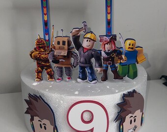 May include: A white cake with a red number 9 on top. The cake is decorated with a blue and white sign that says "R TRIPP" and several Roblox characters.