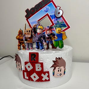 Puede incluir: Una tarta blanca decorada con figuras tem&aacute;ticas de Roblox y un adorno. El adorno presenta el nombre "Josua" y el n&uacute;mero "6". La tarta est&aacute; adornada con recortes de personajes de Roblox y la palabra "ROBLOX" en rojo y blanco.