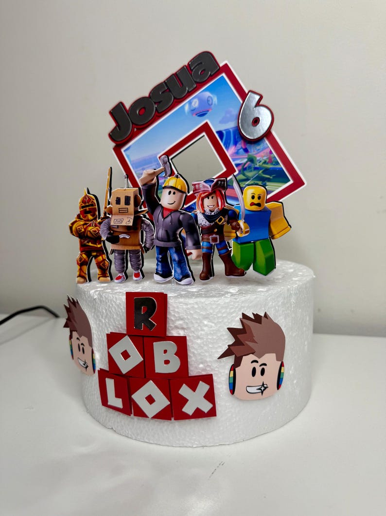 Puede incluir: Una tarta blanca decorada con figuras tem&aacute;ticas de Roblox y un adorno. El adorno presenta el nombre "Josua" y el n&uacute;mero "6". La tarta est&aacute; adornada con recortes de personajes de Roblox y la palabra "ROBLOX" en rojo y blanco.