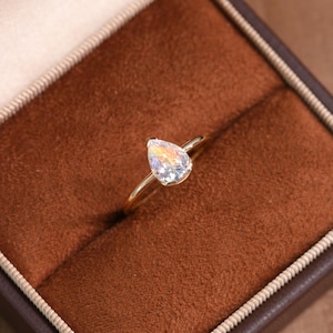 May include: A pear-shaped diamond engagement ring set in a gold band. The ring is in a brown velvet ring box.