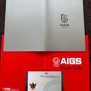 May include: A red folder with the AIGS Gem Lab logo and text. The folder is open to reveal a certificate with Chinese text and a gold seal. The certificate is for a gemstone identification. The folder is on a gray surface.