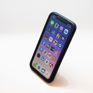 K&ouml;nnte beinhalten: Ein schwarzes iPhone mit einer Schutzh&uuml;lle, das verschiedene App-Symbole auf dem Bildschirm anzeigt. Zu den Symbolen geh&ouml;ren Facebook, Instagram, Twitter, YouTube und mehr.