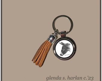 May include: A silver-colored keychain with a round pendant featuring a detailed pencil drawing of a donkey's head. The keychain includes a brown leather tassel. The text "glenda s. harlan c.'23" is below the keychain.