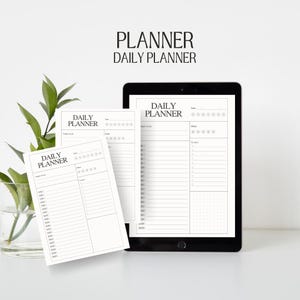 May include: Two black and white daily planner pages with the text "DAILY PLANNER" at the top. The pages are on a white surface with a green plant in a glass vase.