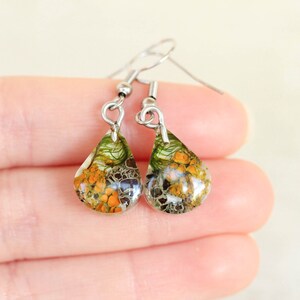 Small teardrop resin earrings with real orange lichen, gray lichen, and green moss, held between fingers to show size. Lightweight and handmade with silver-toned hypoallergenic hooks. Photographed in natural light on a soft background.