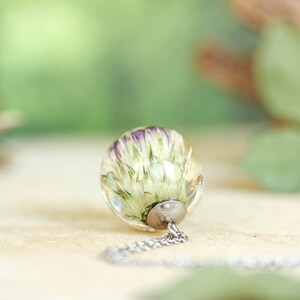 May include: A silver chain necklace with a clear glass pendant containing a preserved white flower with purple accents.