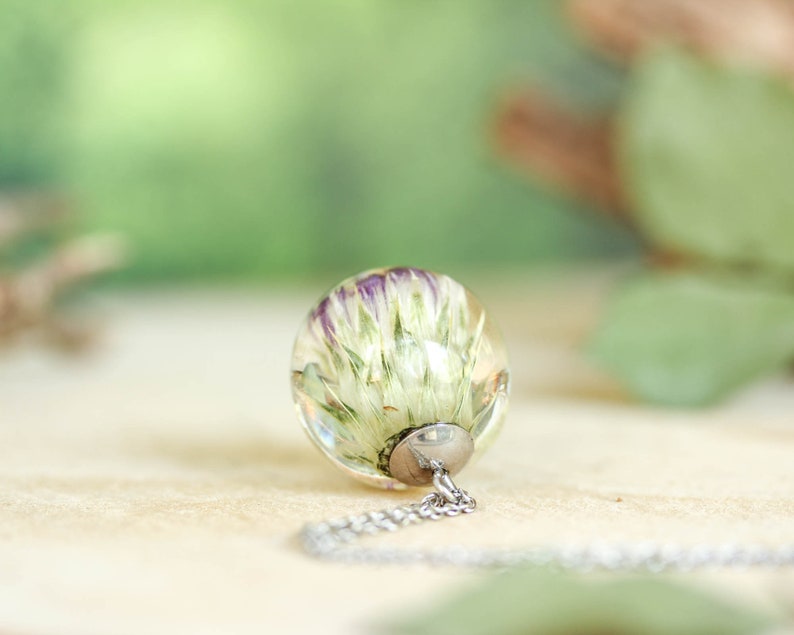 May include: A silver chain necklace with a clear glass pendant containing a preserved white flower with purple accents.