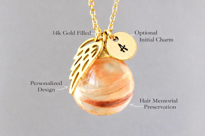 Pode incluir: Colar banhado a ouro com um pingente contendo preserva&ccedil;&atilde;o memorial de cabelo. O pingente &eacute; um globo transparente com mechas de cabelo dentro. Inclui um pingente de asa dourada e um pingente redondo com a inicial "A".
