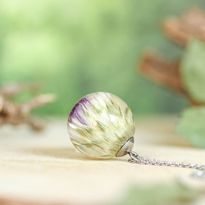 May include: A silver chain necklace with a clear glass pendant containing a preserved flower with purple and green hues.
