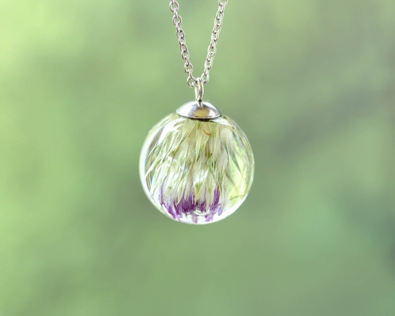 May include: A silver chain necklace with a clear glass pendant containing a preserved white and purple flower.