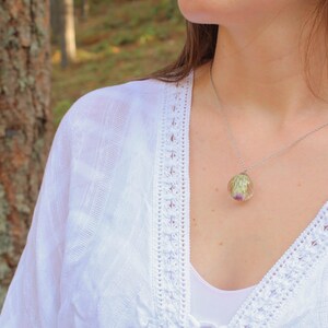 May include: A silver chain necklace with a clear pendant containing a preserved flower. The pendant is round and has a delicate silver chain.