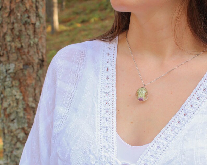 May include: A silver chain necklace with a clear pendant containing a preserved flower. The pendant is round and has a delicate silver chain.